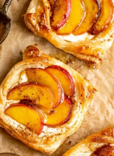 Mini peach and cream cheese tarts served on a white plate, garnished with fresh mint.