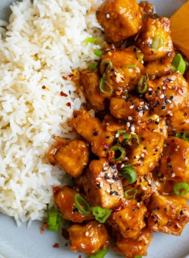 Delicious orange tofu dish garnished with fresh herbs and served in a bowl.