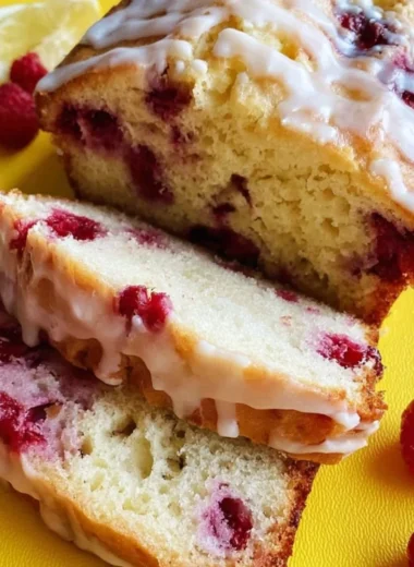 A freshly baked Raspberry Lemon Loaf garnished with raspberries and lemon slices