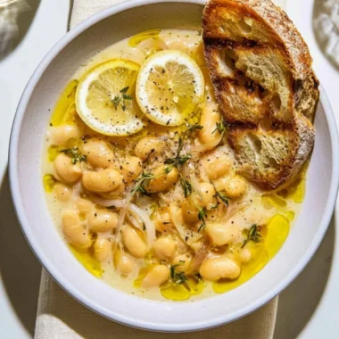 Bowl of brothy white beans garnished with Parmesan cheese and lemon slices